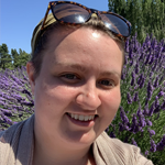photo of Gracie DeMeo, Communications Manager, standing in front of a bush of lavender. 