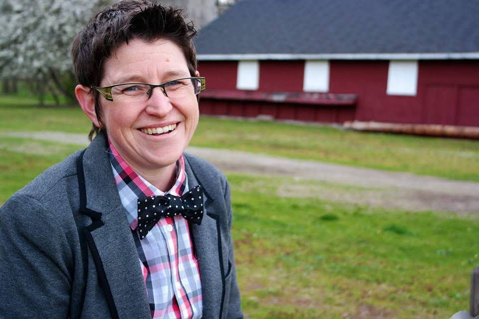 Dana coggin smiles to the camera. There is a barn and grass in the background.