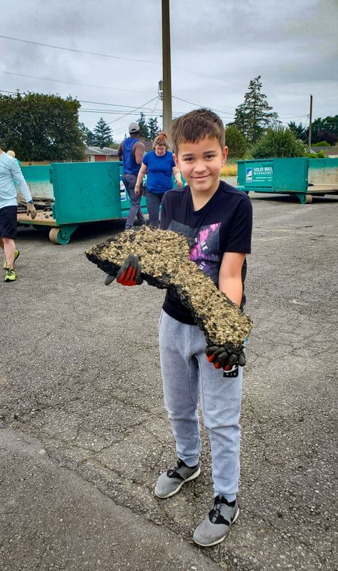 A child volunteer holds a piece of pavement he removed. It’s longer than his torso.