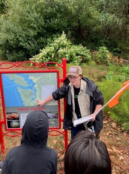 A person with a PCD hat on points at a map of Puget Sound, showing salmon routes to 4th graders.