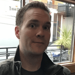 Bryan Mohlman facing forward in front of a window that faces a city street.