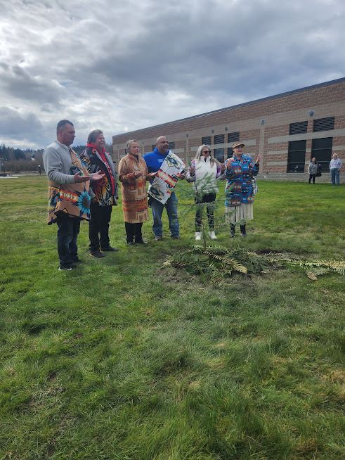 Tribal elders stand in a line and smile, posing with the newly planted tree