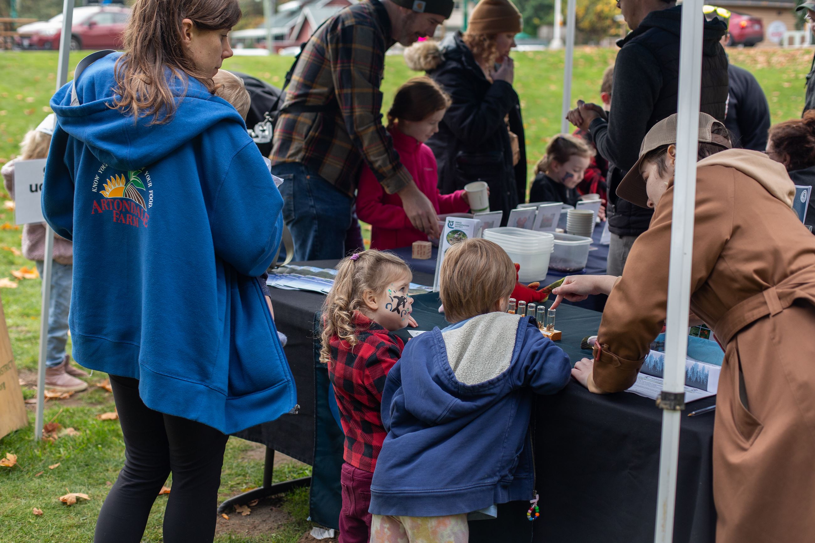 Two kids look at the early salmon life stages vial. PCD worker bends over to explain it to them!