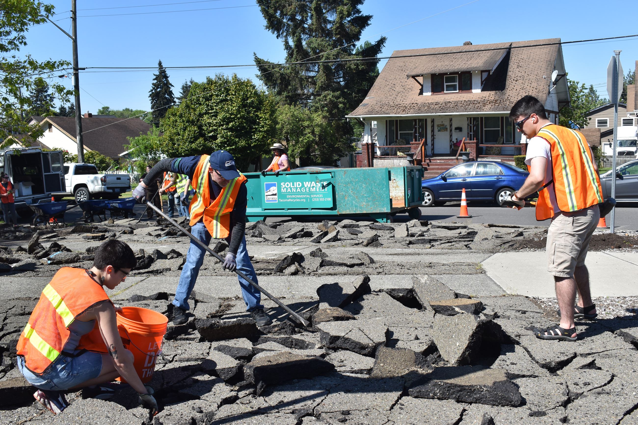 Three volunteers remove pavement using hand tools.