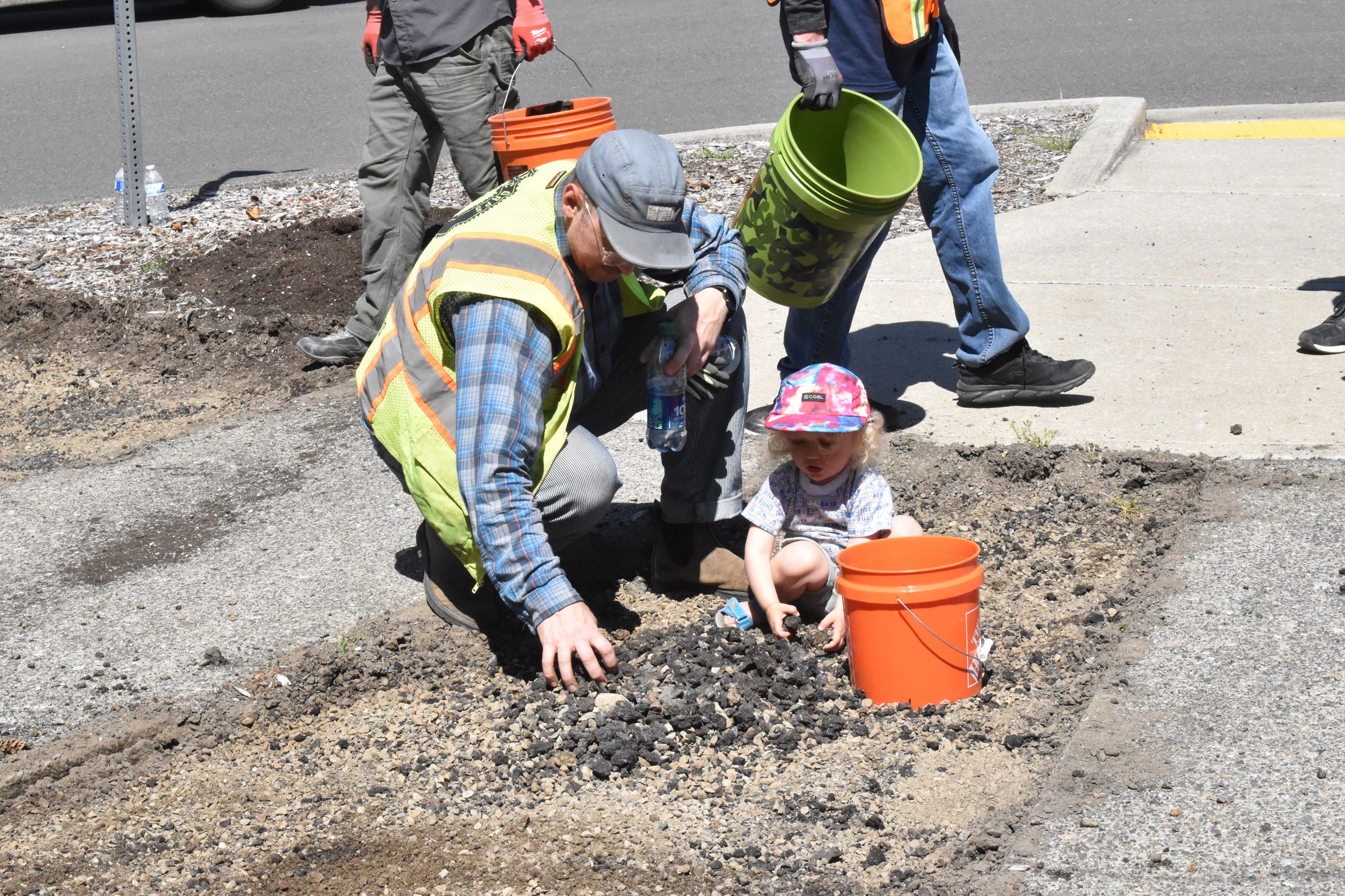 A man and small child pick up small pieces of asphalt.