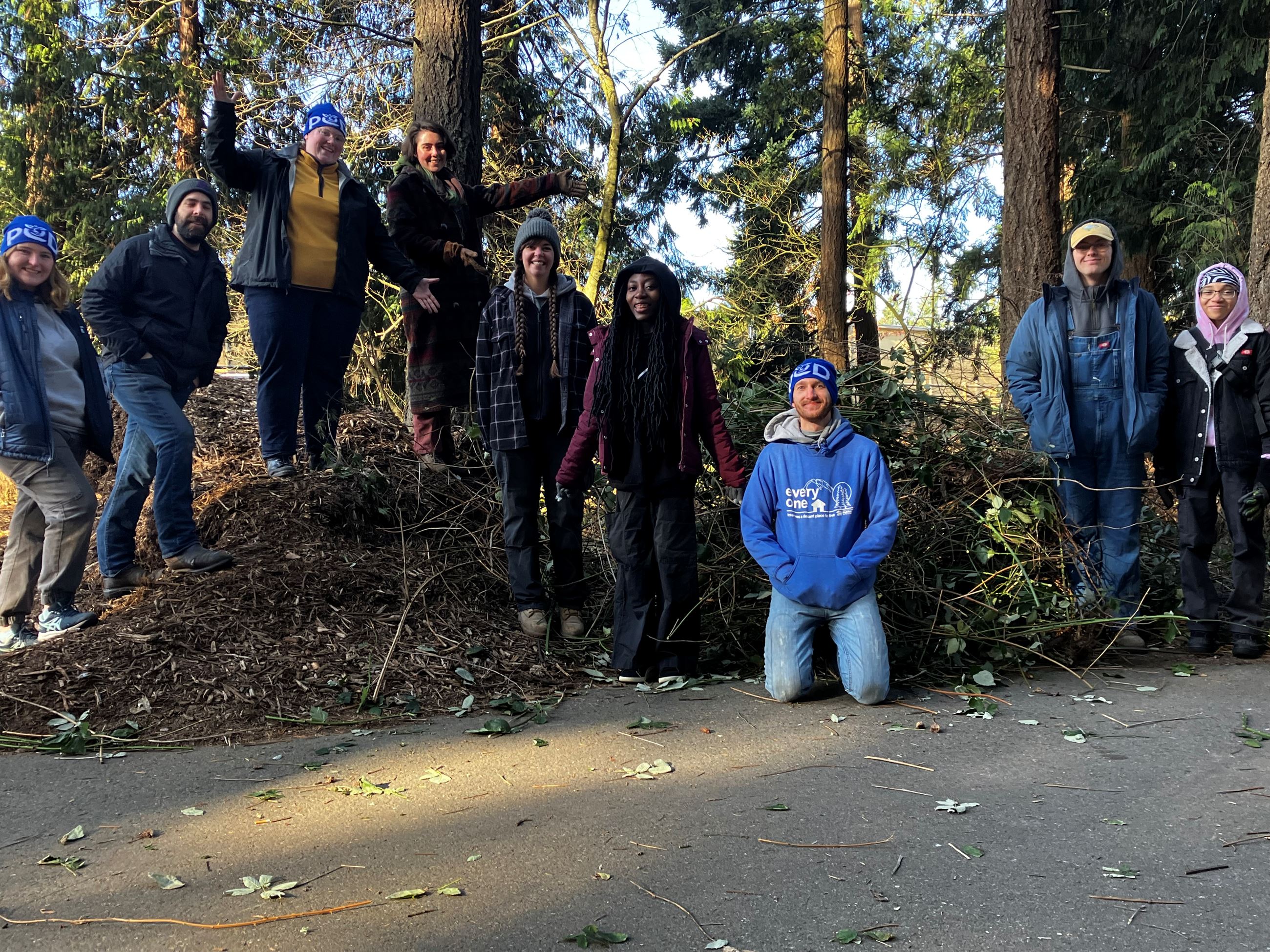 Group of happy volunteers standing on a pile of tree bark and recently pulled blackberry