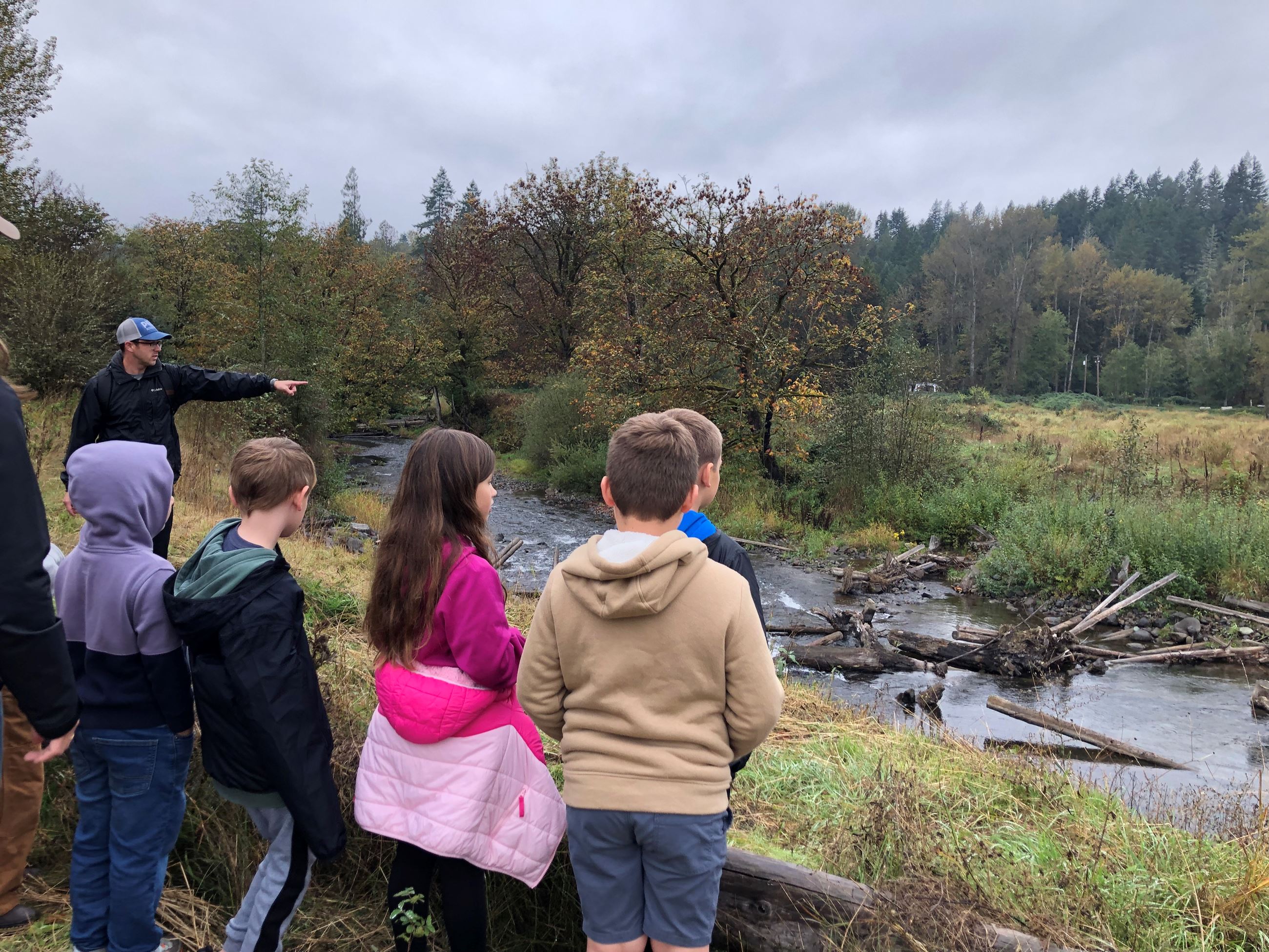 A group of students standing next to South Prairie Creek while educator Chris Towe points.