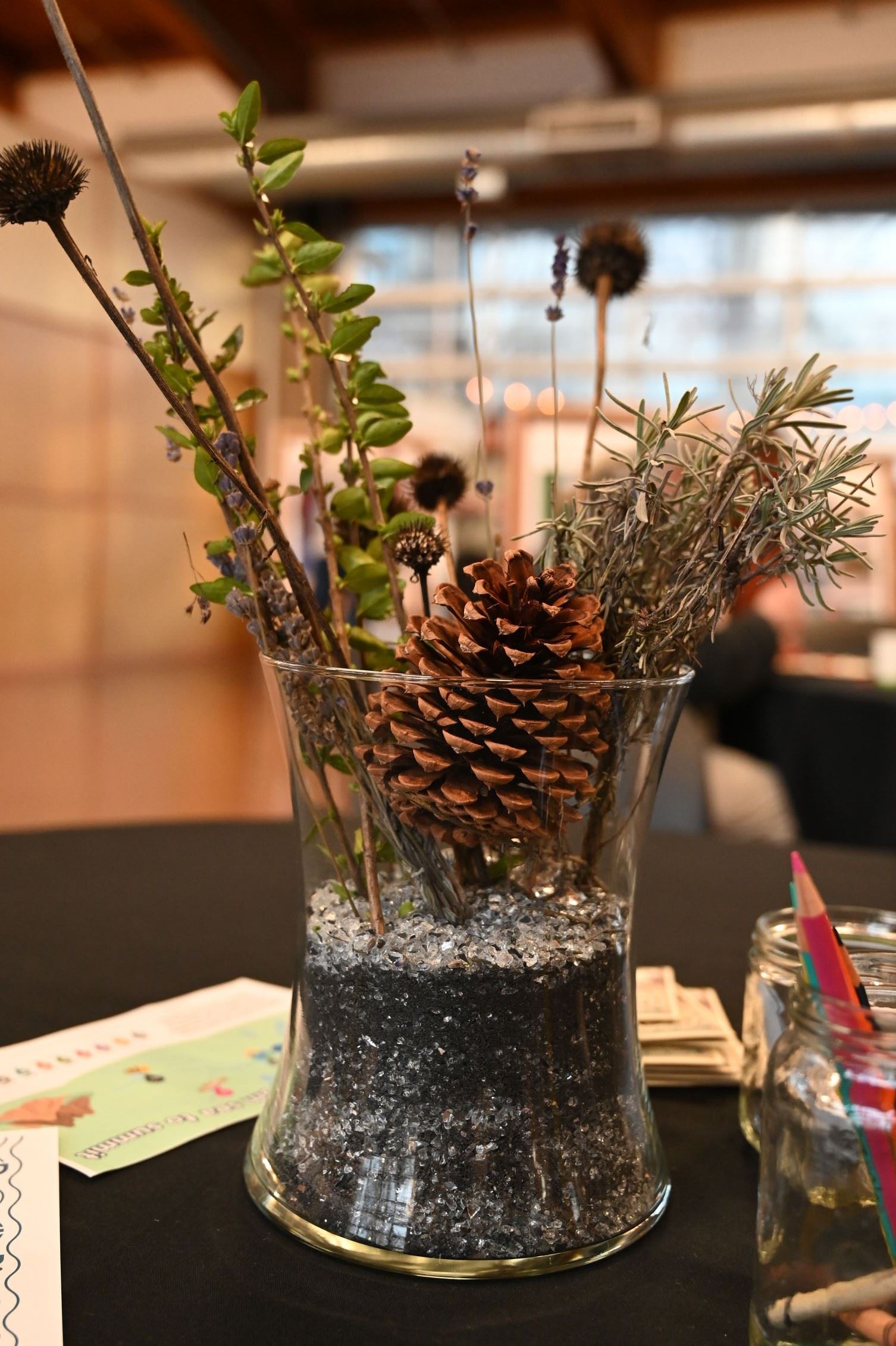 A sandy vase arrangement with stems of native plants and a pinecone