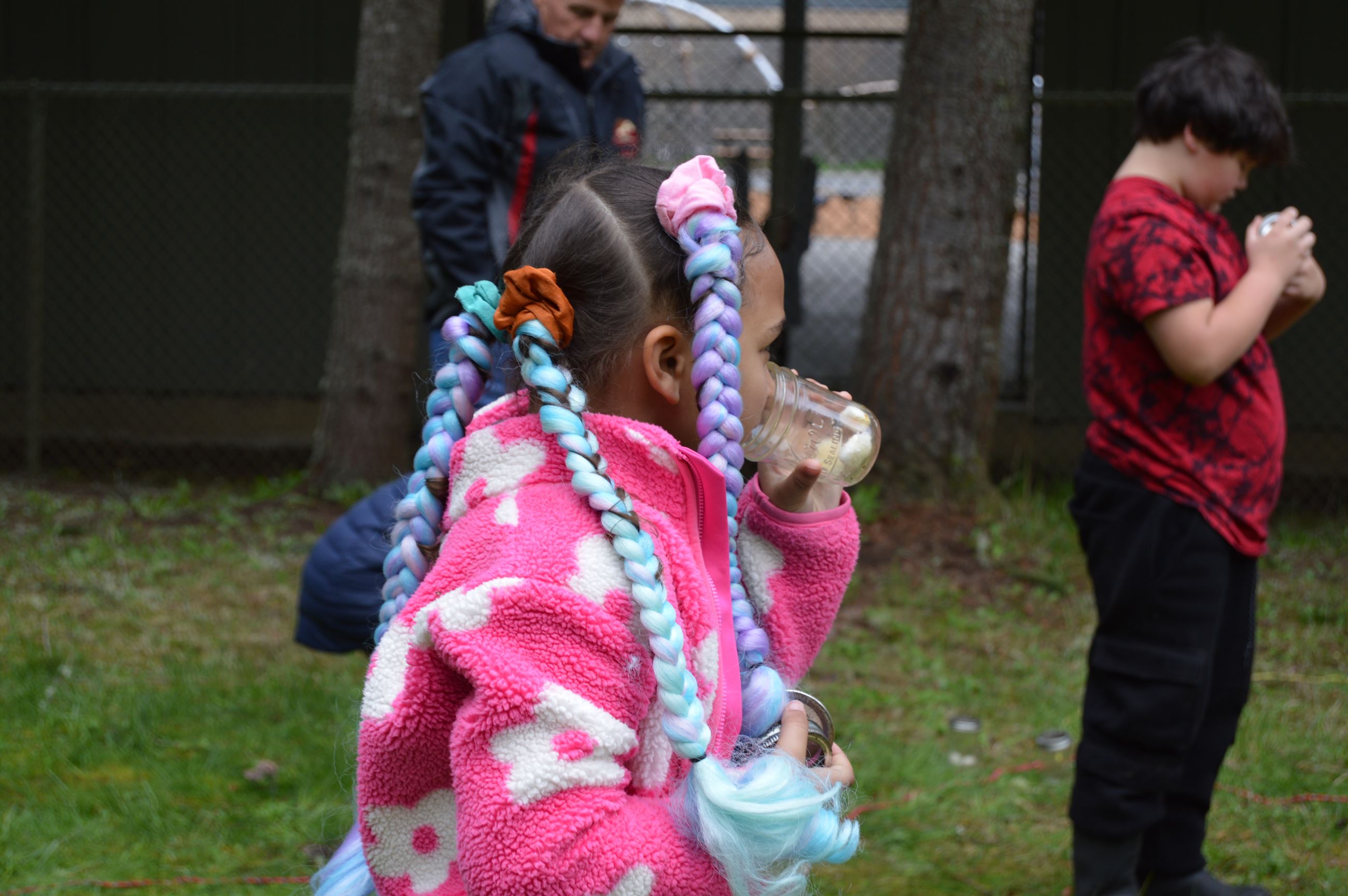 A girl with a pink jacket and blue braids smells a mason jar