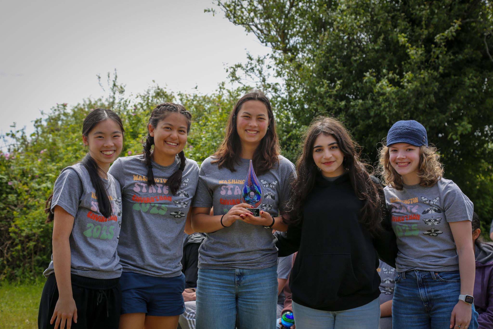 A group of five highschool students stand together in front of trees